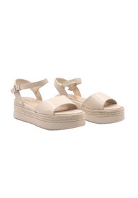 Beige platform sandals with a smooth, faux leather finish. Features cross-strap design, ankle buckle, and textured jute accent on the sole.