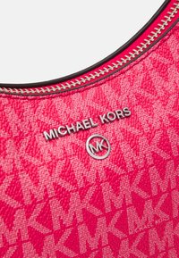 Różowa torba na ramię z płótna, z teksturowanym wzorem i srebrnymi akcentami. Dodatki obejmują zamek błyskawiczny oraz logo "MICHAEL KORS."