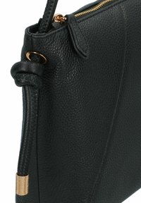 Borsa a mano in pelle nera texturizzata con cerniera dorata e dettaglio decorativo con tracolla annodata.
