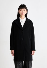 Schwarzer Wollmischungs-Mantel mit Reverskragen, zwei vorderen Knöpfen und Seitentaschen. Entworfen mit einem lässigen Schnitt und glatter Textur.