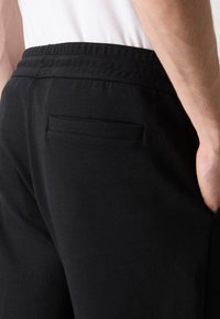 Svarta träningsbyxor med elastisk midja, med en bakficka och en slät yta. Designen är enkel och funktionell.