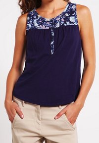 Canottiera blu navy con yoke a motivo floreale, caratterizzata da un dettaglio con bottoni sul davanti e pieghe per un tocco di texture in più. Collo e armhole a costine.