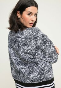 Prošívaná bomber bunda v černé a bílé barvě s texturovaným vzorem, obsahující žebrovaný černý lem s bílými pruhy.