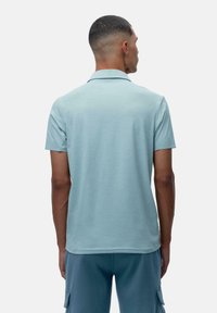 Lyseblå poloshirt med korte ermer og krage, med en glatt tekstur og minimalistisk design. Ingen synlige logoer eller mønstre.