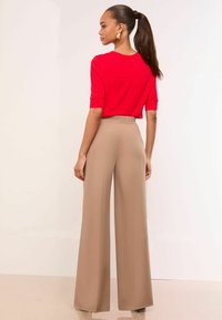 Red short-sleeve top and beige wide-leg trousers. Smooth fabric with a fitted waist. Model has long hair tied back; large gold hoop earrings.