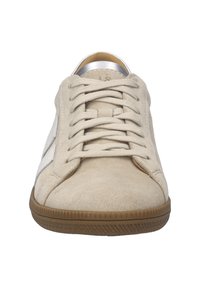 Basket en suedine beige avec une semelle en caoutchouc, à bout rond et lacets plats. Présente un accent en cuir blanc sur le côté et un détail métallique au niveau du talon.