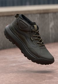 Mørkegrøn sneakers med teksturert overdel, mønstrete såle og polstret krage. Har gulllogo og svarte snøringer for en sikker passform.