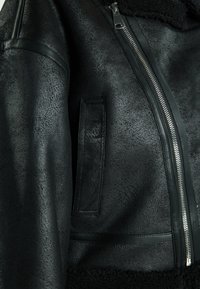 Svart läderjacka med strukturerad yta, dragkedja och en varm fårskinnskrage. Funktioner inkluderar en ficka och släta läderdetaljer.