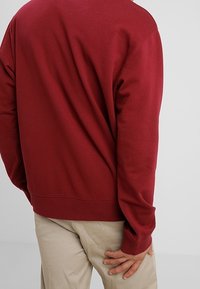 Bordeaux sweatshirts met lange mouwen, een ronde halslijn en een geribbelde zoom. Zacht stof met een gladde textuur. Geen zichtbare logo's of patronen.