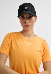Sort kasket med broderet logo, parret med orange sports T-shirt med korte ærmer, der har en subtil tekstur og hvidt brandnavn.