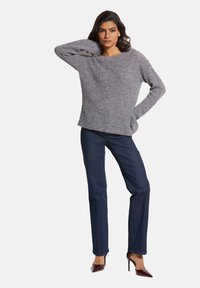 Grauer gestrickter Pullover mit lockerer Passform, Rundhalsausschnitt und umgeschlagenen Ärmeln, kombiniert mit dunkelblauen, geraden Jeans und burgunderroten High Heels.
