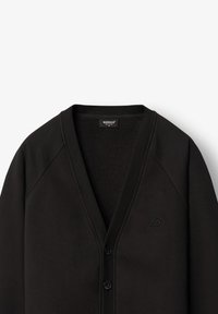 Fekete kardigán puha anyagból, V-kivágással, gombos záródással és bordás mandzsettával. Diszkrét, beleégett logó található a mellkasán.