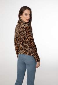 Giacca in pile con stampa leopardo marrone e nera, con colletto alto, maniche lunghe e design aderente, abbinata a jeans in denim blu chiaro.