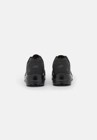Chaussures de sport noires avec une tige synthétique texturée, un talon arrondi et une semelle en caoutchouc épaisse. Présente un logo au talon et aucun élément décoratif.