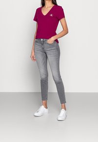 Magenta V-Ausschnitt-T-Shirt mit Logo, kombiniert mit schmalen grauen Jeans und weißen Turnschuhen. Glatter Stoff mit lässiger Passform; minimalistisches Design.