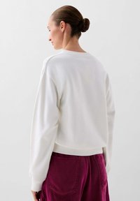 Hanorac alb din bumbac, cu manșete și tiv din tricot, având un croi lejer și guler rotund, asortat cu pantaloni burgundy.