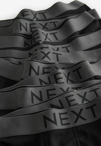 Schwarze Unterwäsche mit breiten grauen Elastikbund, der mit "NEXT" in Schwarz bedruckt ist. Mehrere Hosen übereinander gestapelt, um Textur und Design zu präsentieren.