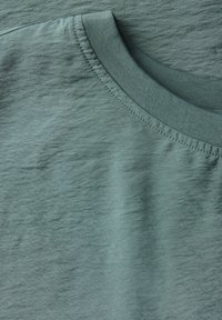 T-shirt in cotone verde chiaro, con una trama liscia, scollatura rotonda e sottili variazioni di colore del tessuto, caratterizzato da un bordo cucito.