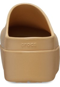 Sabots en caoutchouc beige avec une finition texturée, dos ouvert et plateforme surélevée. Le logo "CROCS" est embossé sur le côté.