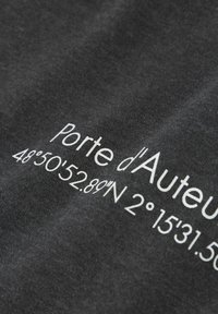 Czarna tkanina z białym napisem "Porte d'Auteuil 48°50'52.89"N 2°15'31.56"E," prezentująca gładką fakturę i wyraźny druk.