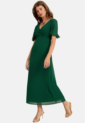 Grünes Maxikleid mit kurzen, rüschenschnitten Ärmeln, einem V-Ausschnitt und dekorativen Knöpfen an der Brust. Kombiniert mit goldenen Sandalen.
