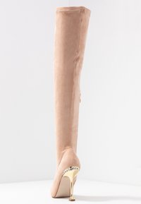 Knähöga beiga mockastövlar med spetsig tå och stilettklack. Klacken har en metallisk guldbas prydd med rhinestones.