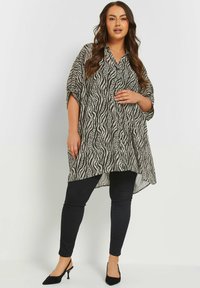 Camicia a maniche lunghe, svasata, in un motivo a onde bianco e nero, abbinata a jeans skinny neri e tacchi a spillo neri. Tessuto morbido.