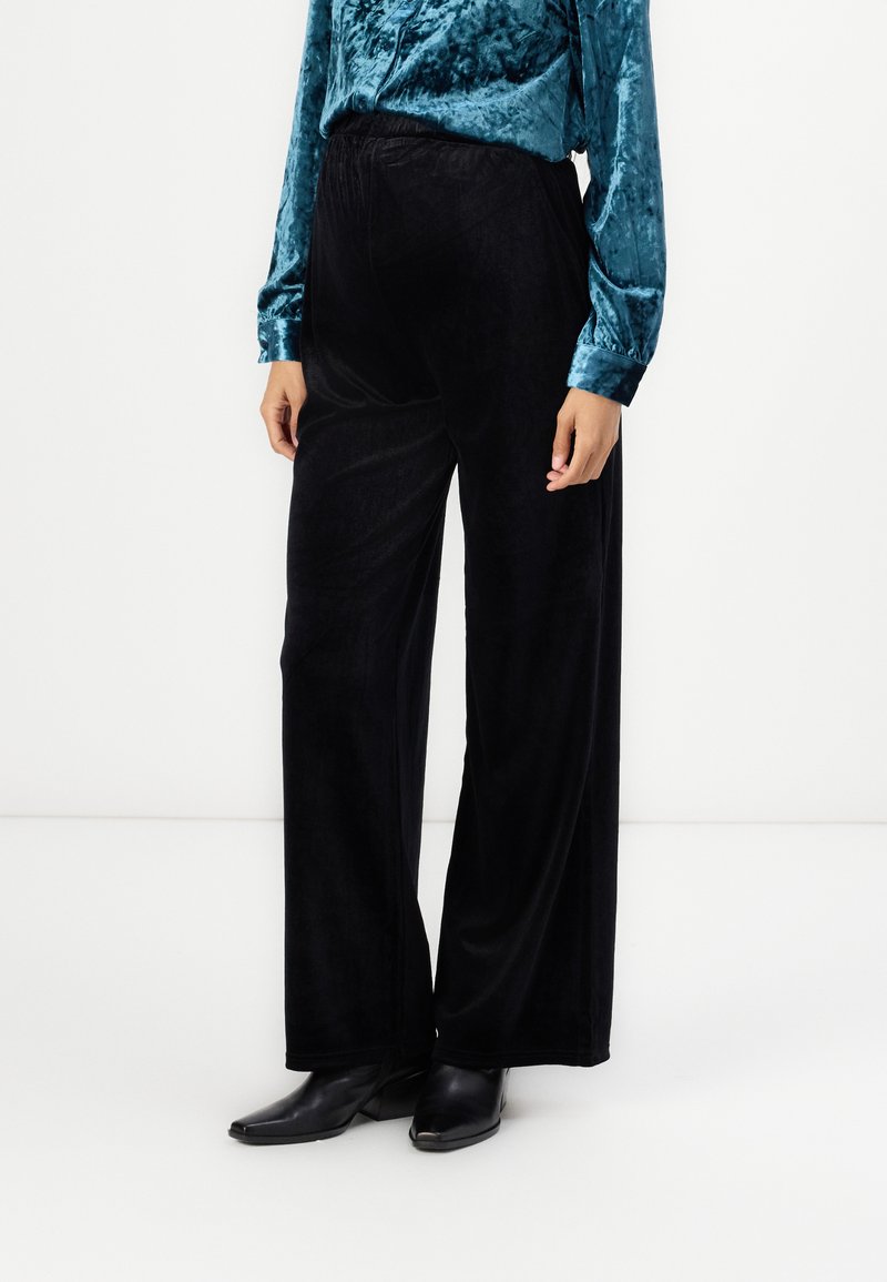 Black, wide-leg velvet pants with an elastic waistband. The texture is soft and shiny, paired with a teal velvet blouse. Footwear is black boots.
