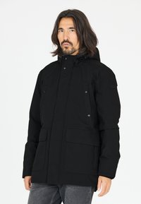 Sort vandtæt jakke med hætte, fronttryklåse og to store frontlommer. Materialet ser glat og holdbart ud.