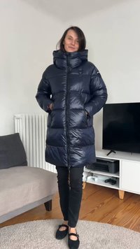 Długa granatowa kurtka puchowa z wysokim kołnierzem, zamkiem błyskawicznym i bocznymi kieszeniami. Charakteryzuje się błyszczącą fakturą i prostokątnym krojem zapewniającym ciepło.