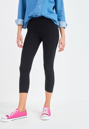 Mustad mustad capri leggingud venivast kangast, koos teksashirtiga. Kandmiseks erksate roosa värvi madala profiiliga tennisetega. Omab keskmist tõstet.