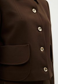 Brun kavaj med en slät textur, utrustad med knappar i guldton, en ficka med lappar och en skräddarsydd krage.