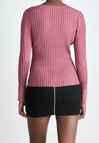 Rosa gerippte Langarmbluse mit einem runden Ausschnitt, kombiniert mit einem schwarzen Minirock mit einem Reißverschluss auf der Rückseite.