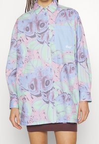 Hemd mit Knopfleiste in einer pastellfarbenen Palette, verziert mit einem verspielten Muster aus Schmetterlingen und Blättern, langen Ärmeln und einer Brusttasche in Hellblau.