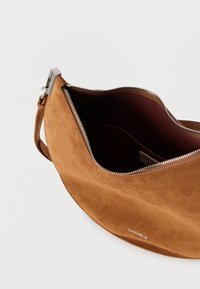 Ruda zomšinė peties rankinė su lygiu paviršiumi, sidabrine užtrauktuku ir tamsiai bordo vidumi. Priekyje yra logotipas.