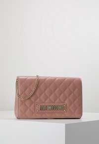 Prošívaná růžová kabelka ze syntetické kůže se zlatým řetízkem a logem. Obdélníkový tvar s uzávěrem na klapku a detailem v podobě diamantového vzoru.
