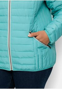 Lehká tyrkysová prošívaná bunda s vertikálním šitím, dvěma postranními kapsami na zip a stříbrným předním zipem. Měkký nylonový materiál.