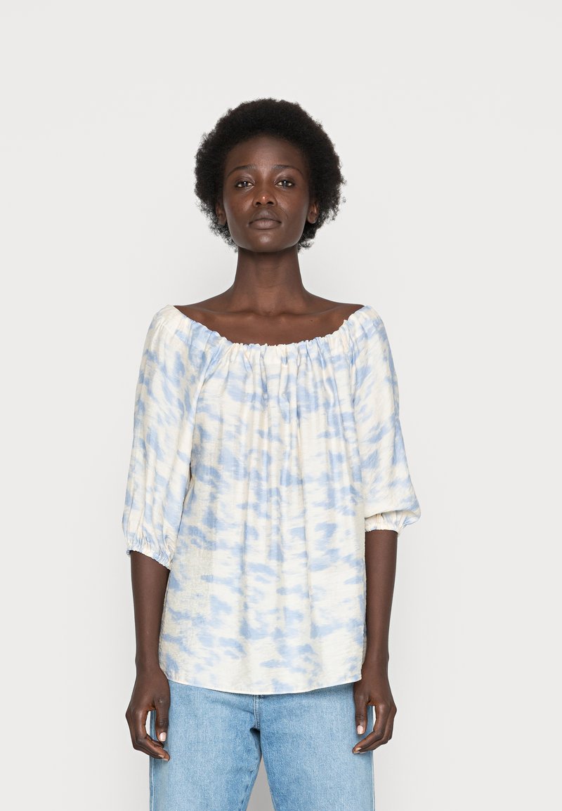 Blusa leve, com ombros à mostra, em um padrão de tie-dye azul e branco. Apresenta mangas de três quartos com punhos elásticos e um ajuste relaxado.