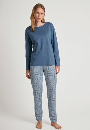 Blaues Langarmshirt kombiniert mit hellblauen, gemusterten Schlafanzughosen, die ein geometrisches Muster mit roten und dunkelblauen Akzenten aufweisen.