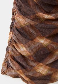 Gros plan d'un tissu à carreaux marron et orange froncé avec une texture visible et une couture le long d'un bord.