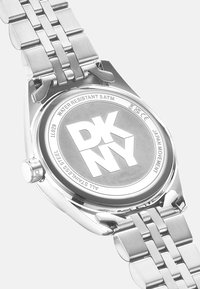 Orologio in acciaio inossidabile con bracciale in metallo. Il fondo della cassa rotonda presenta il logo "DKNY" e dettagli sulla resistenza all'acqua. Finitura lucida.