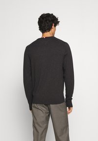 Maglione lavorato a maglia grigio scuro con maniche lunghe, polsini e orlo a costine, e una piccola etichetta colorata sul retro del collo. Tessuto morbido, vestibilità standard.