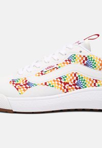 Baskets Vans blanches avec motif tourbillonnant à damier multicolore sur les côtés, lacets blancs et étiquette rouge du logo Vans près des lacets.