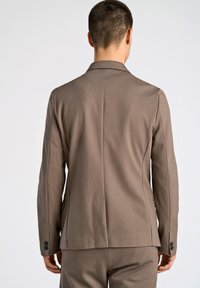 Blazer marrón ajustado con una textura suave, ajuste estructurado, diseño de un solo botonadura y dos botones en los puños, visto desde atrás.
