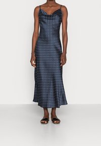 Robe en satin bleu marine à pois, avec un décolleté plongeant, des fines bretelles et un ourlet fluide, associée à des sandales à glisser noires.