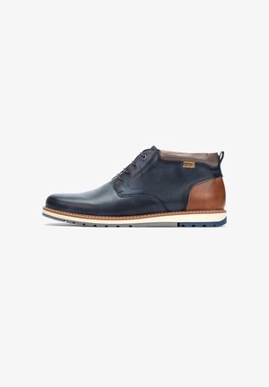 Bottes chukka pour hommes en cuir bleu marine avec des accents en cuir brun, lacets rouges, semelle en caoutchouc blanche et coutures contrastantes.
