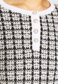Cardigan con bottoni realizzato in tessuto texturizzato bianco e nero con un motivo a scacchi. Tre bottoni simili a perle con dettagli dorati.