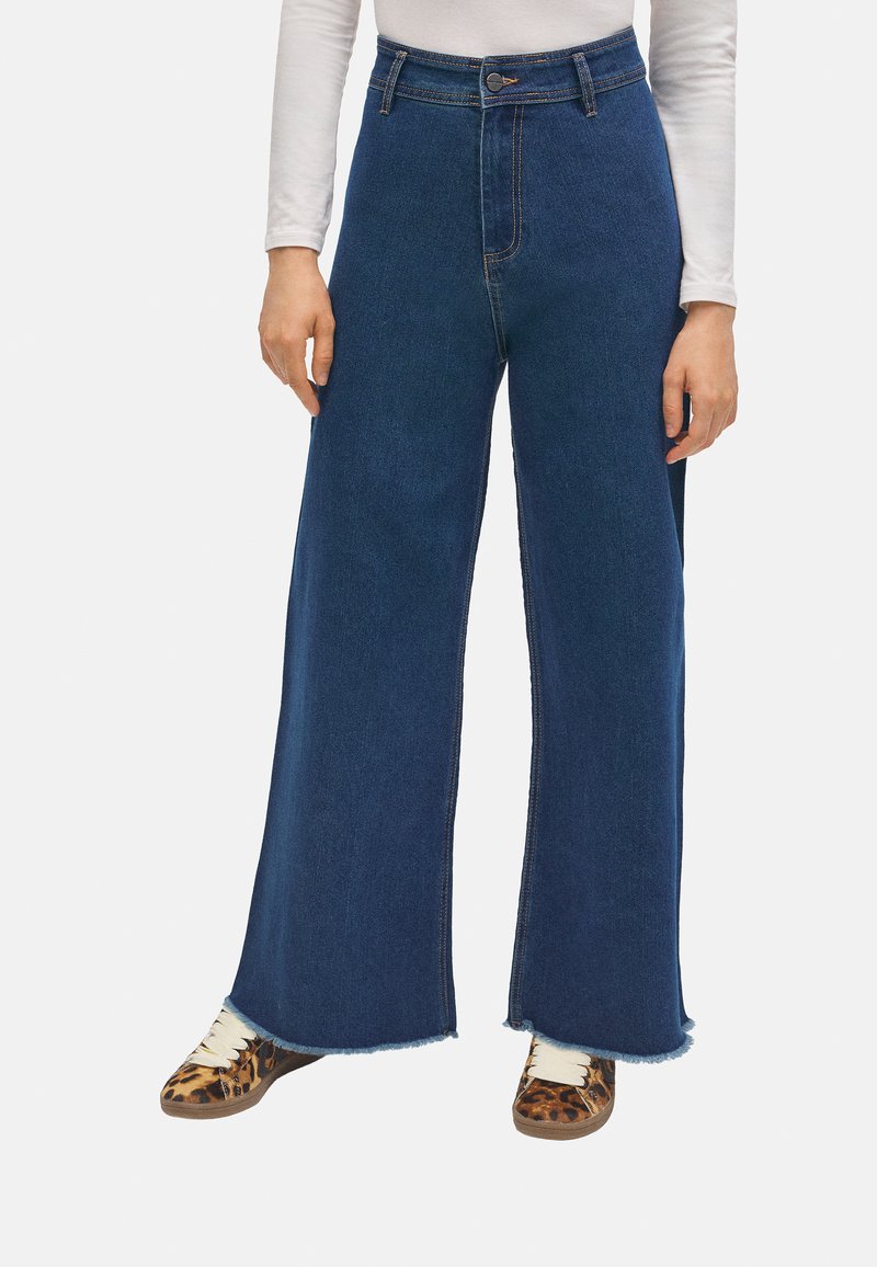 Jeans de tiro alto y pierna ancha en denim azul oscuro con dobladillo sin rematar. Combinados con zapatillas de estampado animal, que tienen cordones en beige y suelas texturizadas.