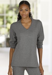 Pelēks v-veida kakla džemperis ar garām piedurknēm, mīksta tekstūra un brīvs piegriezums, kombinēts ar saskaņojošiem pelēkiem apakšdaļām. Vienkāršs dizains, bez redzamām rakstām.