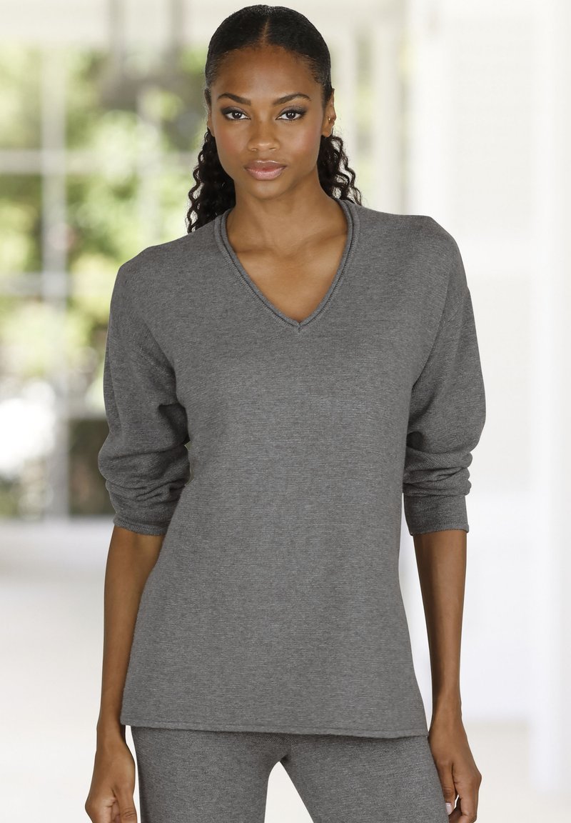 Pelēks v-veida kakla džemperis ar garām piedurknēm, mīksta tekstūra un brīvs piegriezums, kombinēts ar saskaņojošiem pelēkiem apakšdaļām. Vienkāršs dizains, bez redzamām rakstām.